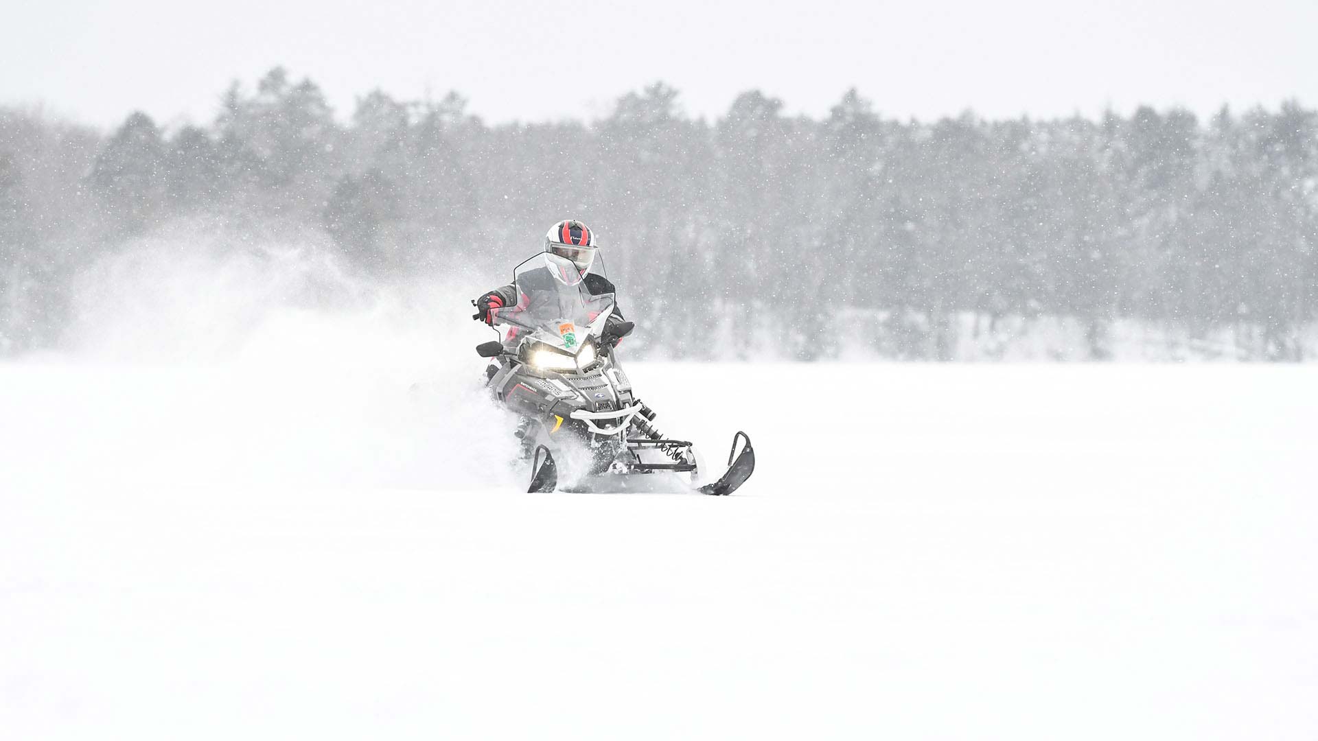 A snowmobiler kicking up powder as he rides one Boulder Lake